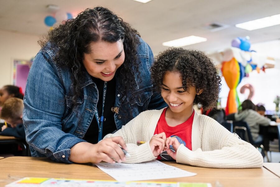 Hispanic teacher leaning over hispanic girls shoulder to help with homework